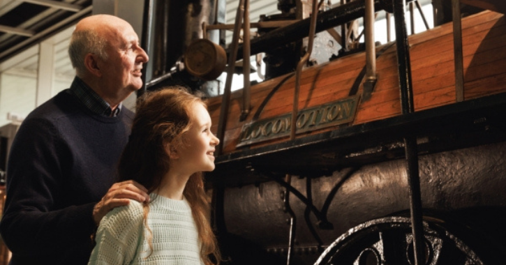older man and small girl smiling looking at Locomotion historic engine inside Locomotion Railway Museum